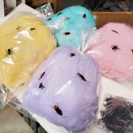 Four bags of cotton candy in yellow, blue, purple, and pink with spider and cockroach decorations on top.