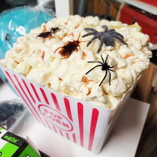 A popcorn container filled with popcorn is topped with four fake spiders of varying sizes and colors.