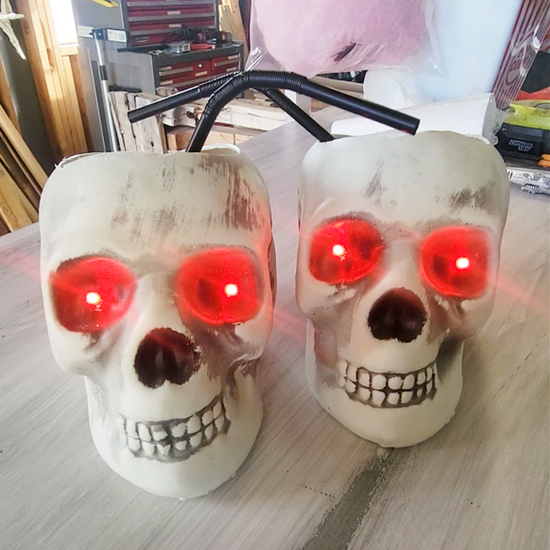 Two skull decorations with glowing red eyes and black wires protruding from the top are displayed on a wooden surface.