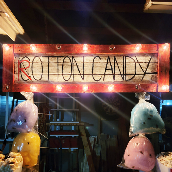 Colorful bags of cotton candy under a lit wooden sign that reads 