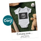 Flat lay of a baby onesie with a sonogram print, surrounded by a teddy bear, baseball, bat, and glove, on green turf. Text reads "Coming soon... Baby Baker Due January 2026.