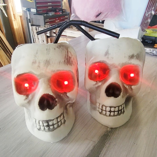 Two skull drinks with glowing red eyes and black straws on a table.